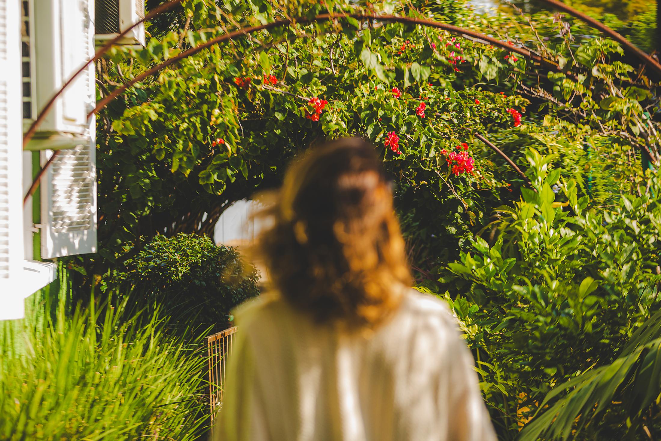 Mulher caminhando entre plantas e flores em um jardim da Zona Sul